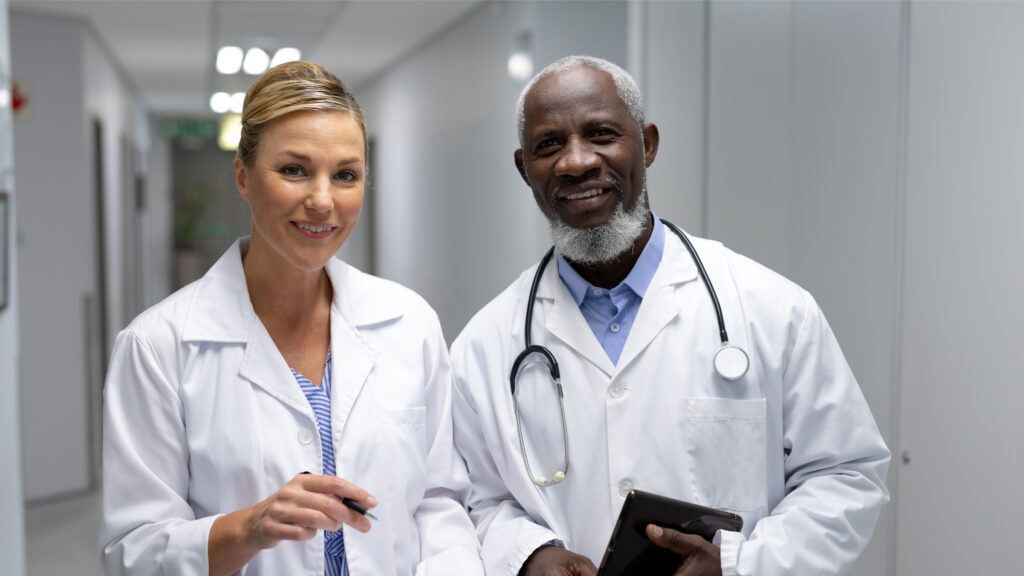 A male and female doctor standing side by side in a hospital hall.