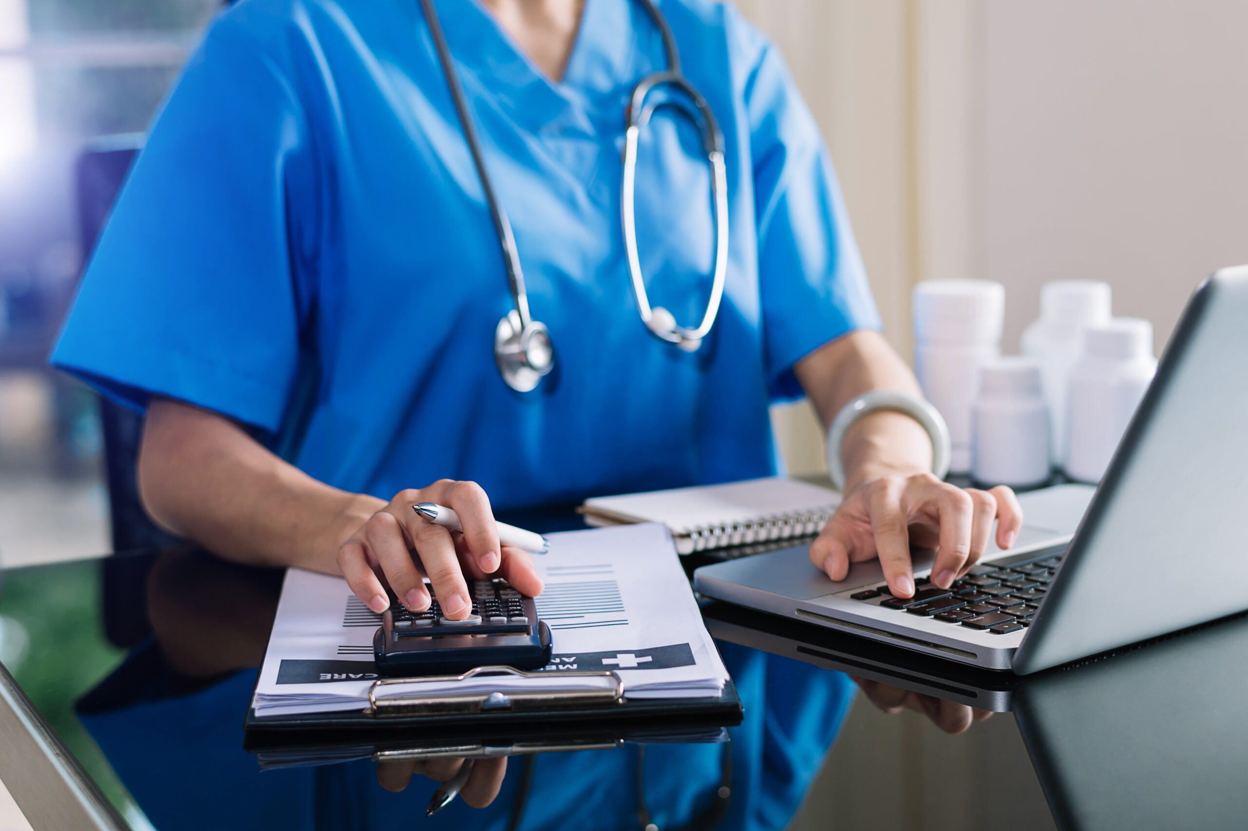 Healthcare professional using calculator and laptop